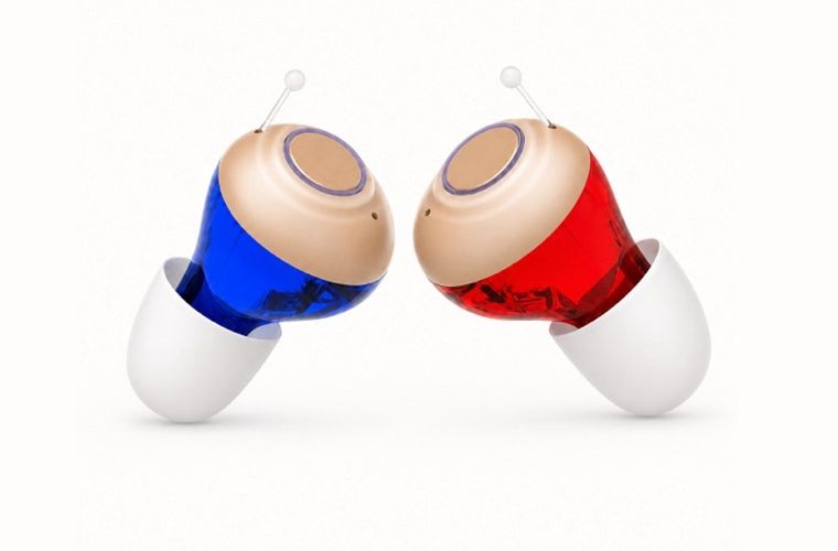 Two in-the-canal hearing aids with soft ear tips, blue for the left ear and red for the right